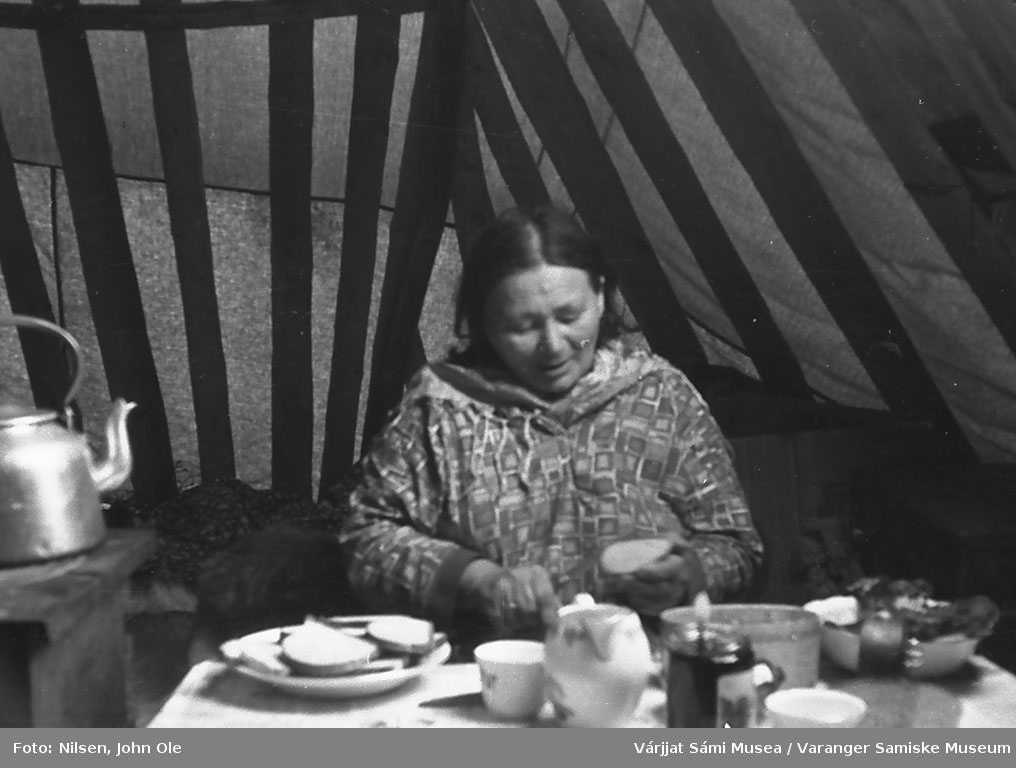 En kvinne sitter i lavvoen og smører brødskiver. Kåfjord 1966.