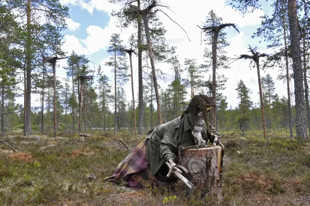 Trollkjerring lagd i tre lener seg over en trestubbe ute i skogen.