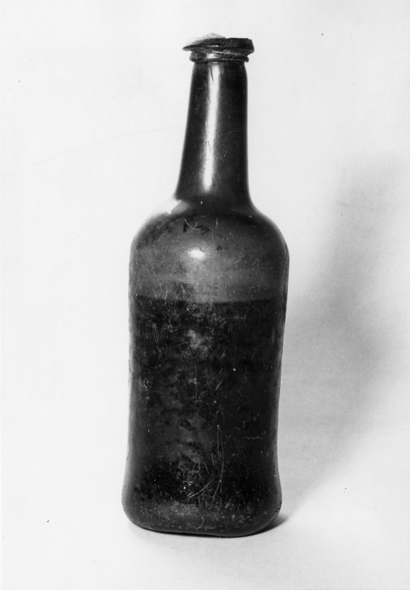 Vinflaska av mörkgrönt glas, delvis fylld med vätska.