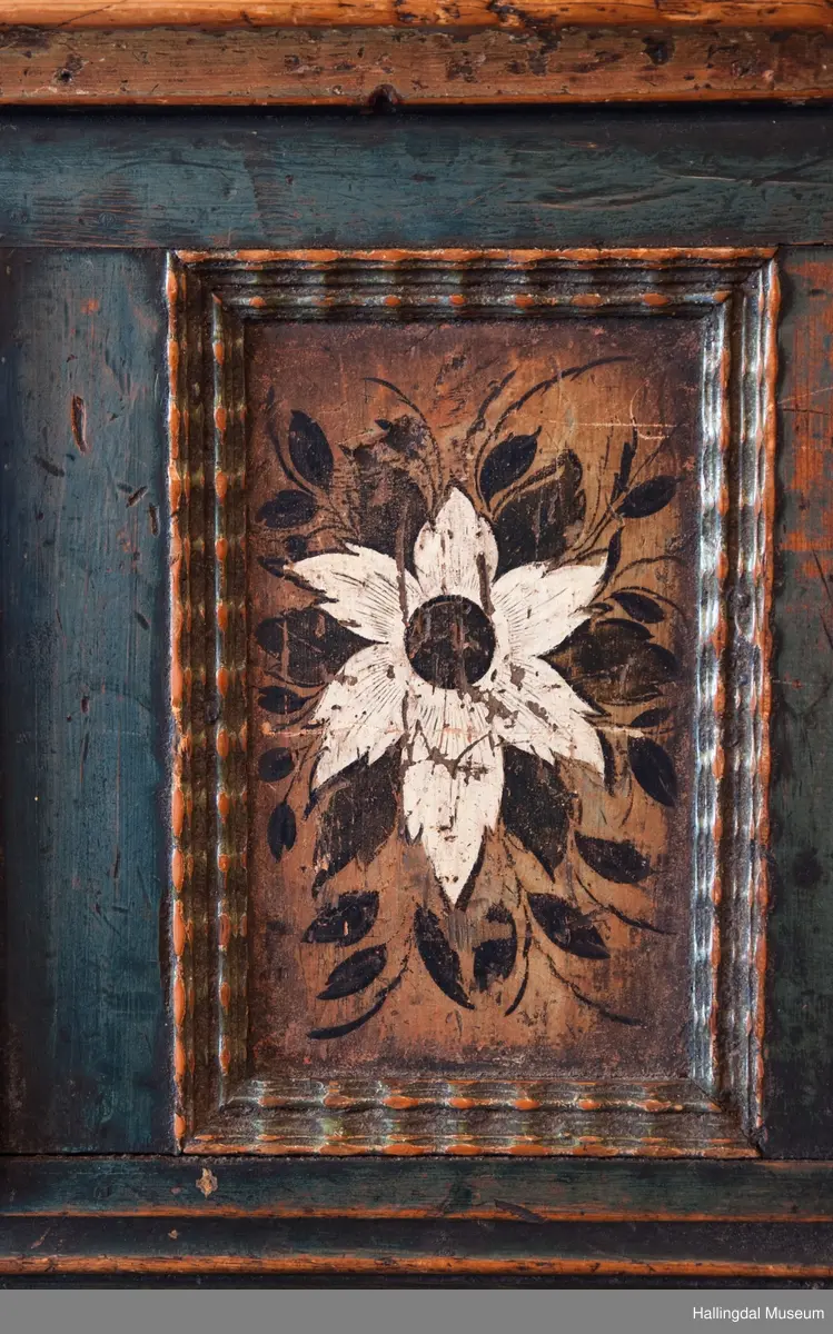 Delene satt sammen v.hj.a. tapping og trenagler.  Gavlen buede sider med skåret kronlist, delt i 3 profilerte, med opprullede ender.  Kronlister fortsetter på sidestykkene.  I toppen av kronlist hjerteformet, gj.brutt utskjæring opp ned.  Gavlens sentralfelt utskjæring i dyp flatskurd.  To løver, vendt mot hverandre, griper om hellebordskaft.  En stake som øverst kløyves i to bjørnehoder i profil skiller løvene.  Gavlen (el. baldakinens) forplate danner fremsiden i skuff i skapets bredde og dybde.  Overskapet:  Åpen hylle øverst, ca. 25 cm høy.  Under hyllen er det delt i 3 felt.  Ett skap i hvert sidefelt.  Midtfeltet har 2 skuffer adskilt av åpen hylle.  H. Skuffe: 12,5 cm.  H. åpent rom: 17 cm.  Under nederste skuff, skap med skråsider som stikker ca. 15 cm ut fra forveggen på overdelen.  Skapet dekkes av liggende skråklaff.  Festet jrenbeslag og hengsler nederst.  
En stor skuff i hele skapets bredde, 6 cm høy nederst, 32 cm dyp.  Over skuffen er rommet delt i 3 felt.  Hvert sidefelt har 2 skuffer og midfeltet en dyp skuff.  Midskuff har fylling med utskåret medaljong, klaff og hylle og skuffen rødmalt. .................................................