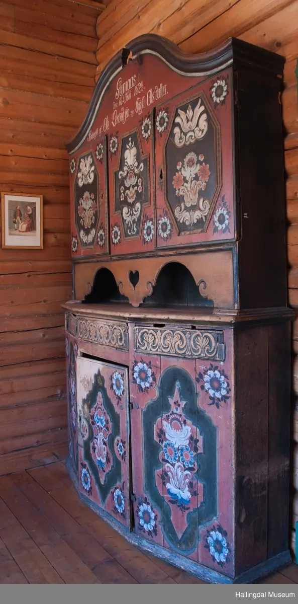 Delene festet med trenagler.  Høy, buet gavl med fremspringende kronlist som øverst har gjennomskåret omvendt hjerte.  Kronlist har hulkil og vulst, og fortsetter på sidene av overskap.  Overskapets front delt i tre felt, med en dør i hvert sidefelt.  Dørene er hengslet til skapets sider.  Hengslene av jern og festet på overkant og underkant av skap og på overkant og underkant av ramme.  Dørene har to profilerte labanker i spor på innsiden.  Låskasetter innfelt i dørblad.  Låsskiltene mangler.  Nøkkel med kløverformede hoder, profilert. En skillevegg midt i overskapet.  To hyller i hvert skap.  Dørene og midtfelt har speil med fyllinger og utskjæringer, akantus i relieff på speilflatene.  Dørspeilene er ovale, åttekantede.  Speil i midtfelt har tilnærmet korsform.  Skjenken har utskåret forplate, i tunger.  Under midfelt får forplaten helt ned til skjenkeplate med gjennombrutt hjerte.  Halvrunde åpninger i hver side. ..........