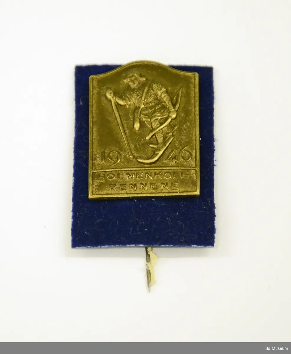 Pin med innskrift:
"HOLMENKOLLRENNENE 1946" og "birkebeiner"
Messingplate montert på plate med blå plastplate med "fløyel" (og nål)