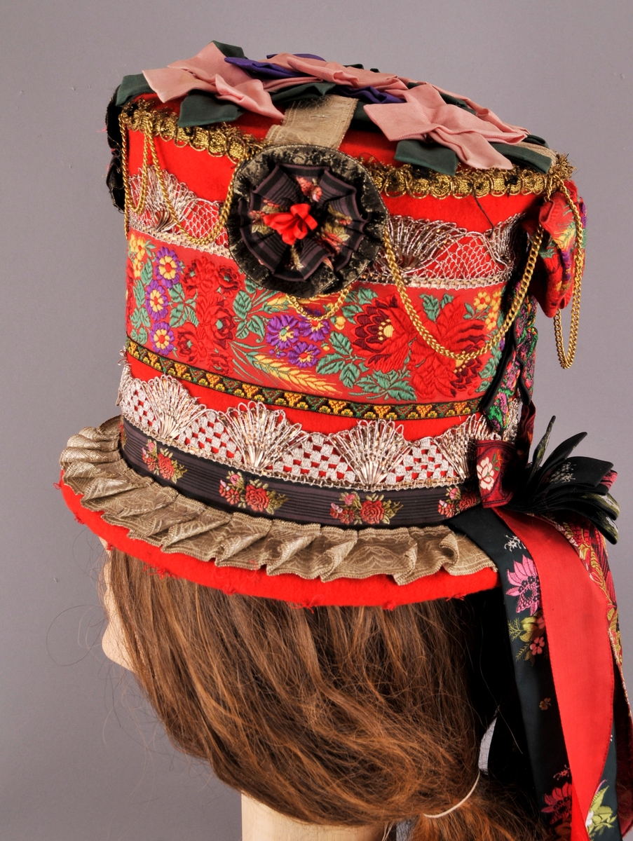 Brudehatt, nylaga. Oppbygd rundt ein filthatt av Zinkes mote AS. Langs bremmens ytterkant er det lagt ei "pølse" av vatt før heile hatten er kledd med høgraudt klede med tydleg lerretsvev. Inni går den raude kleden litt over halvvegs opp i hatten. Der er det  sydd ein løpegang med eit band til å dra saman vidda med, dette for at hatten skal slutte betre rundt hovudet. 
På bremmens overside er ei sylvbore foldelagt og sydd fast langs innerkanten, denne bora er truleg ikkje ny. Vidare rundt hattens pull er det sydd fast eit band med lansert blomemønster, ein sylvknipling, eit smalt band med brodsjert mønster og ein sylvblonde (ulik den som er lenger ned) og til slutt ei avklypt gullblonde/agraman heilt på toppen av pullens kant. Banda er i ein blandingskvalitet.
Over pullens topp (flat del) er ei sylvbore lagt i kryss, over denne er det festa rosettar sydd av grønt, lilla og rosa syntetisk band. Langs kanten av pullen er det sydd fast 3 rosettar, ein midt framme og ein på kvar side. I tillegg er eit "gull"-kjede av uedelt metall sydd fast så det heng i ujamne bogar.
Midt bak på hatten er det øverst sydd fast ei sløyfe av eit lansert bomullsband og ei mindre sløyfe nederst av eit mønstervove band. i tillegg ni lange heng av band, både einsfarga og mønstervove.