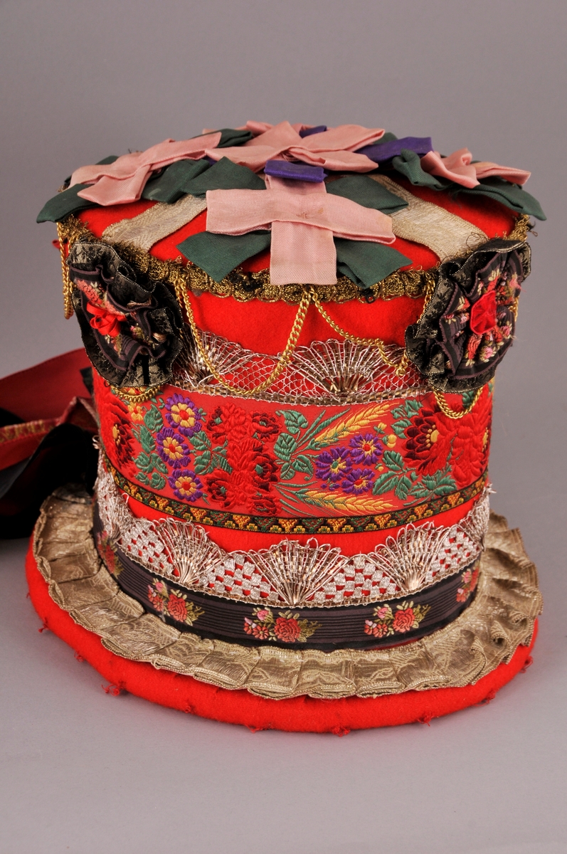 Brudehatt, nylaga. Oppbygd rundt ein filthatt av Zinkes mote AS. Langs bremmens ytterkant er det lagt ei "pølse" av vatt før heile hatten er kledd med høgraudt klede med tydleg lerretsvev. Inni går den raude kleden litt over halvvegs opp i hatten. Der er det  sydd ein løpegang med eit band til å dra saman vidda med, dette for at hatten skal slutte betre rundt hovudet. 
På bremmens overside er ei sylvbore foldelagt og sydd fast langs innerkanten, denne bora er truleg ikkje ny. Vidare rundt hattens pull er det sydd fast eit band med lansert blomemønster, ein sylvknipling, eit smalt band med brodsjert mønster og ein sylvblonde (ulik den som er lenger ned) og til slutt ei avklypt gullblonde/agraman heilt på toppen av pullens kant. Banda er i ein blandingskvalitet.
Over pullens topp (flat del) er ei sylvbore lagt i kryss, over denne er det festa rosettar sydd av grønt, lilla og rosa syntetisk band. Langs kanten av pullen er det sydd fast 3 rosettar, ein midt framme og ein på kvar side. I tillegg er eit "gull"-kjede av uedelt metall sydd fast så det heng i ujamne bogar.
Midt bak på hatten er det øverst sydd fast ei sløyfe av eit lansert bomullsband og ei mindre sløyfe nederst av eit mønstervove band. i tillegg ni lange heng av band, både einsfarga og mønstervove.