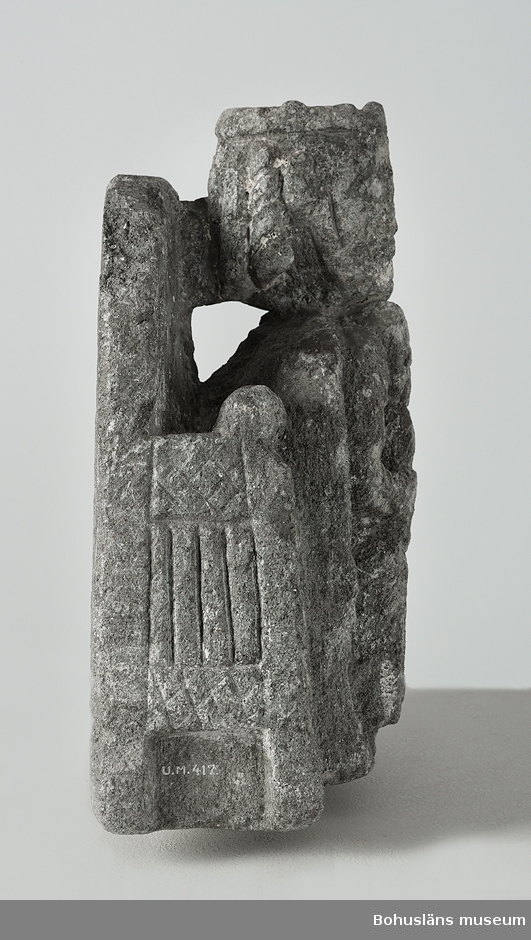 Stenskulptur av täljsten från Svarteborgs kyrka. Den helige Olof sittande i tronstol med högt ryggstöd. Han bär livbälte och mantel, en murkrona på huvudet, möjligen ett relikvarium i höger hand och håller vänster hand om skägget. Skulpturen är starkt eroderad.

Ur handskrivna katalogen 1957-1958: Olav d. helige, täljsten, Svarteborg. M: H. 41, största Br. 32,5 cm; krona och mantel, i höger hand spiran, vänster griper om skägget; sittande på en tronstol m. armstöd och högt ryggstöd, på alla håll smalnar stolen av uppåt. Starkt sliten.

Ur Katalog 1. Uddevalla Museihistoriska samlingar, svenska avdelningen. A. Yngre föremål. Upprättad av Knut Adrian Andersson 1916:                                                                                                                              No 34. Bild i täljsten av Olov den Helige. Yngre medeltiden, räknad till 1550. Förvarats i Svarteborgs kyrka under namnet "Kung Rane". Skänkt av församlingen år 1860-70-tal till Uddevalla museum. Förvaras ovanpå Medeltidsskåpet i sydvästra rummet.

Presenterad i  Uddevalla Museums tryckta katalog 1869 under rubriken 
F] Saker från yngre Medeltiden, räknad till 1550.
N:o 1. Bilder af S:t Olof i sten från Svarteborgs kyrka.

1861-1870 1 Arkeologiska och Etnografiska samlingarna U-a Museum D4A 1
Ur Gåvobok1864:
Svarteborgs församling:
Kristusbild af träd samt fragmenter af en Granit- [överstruket] Täljstensbild, enligt sägen föreställande Kung Rane, hvilka begge setat [överstruket] [oläsligt tillägg] i Svarteborgs kyrka. 
Tillagd kommentar av intendent Knut Adrian Andersson; Olof d. Helige troligen.

Se foton på föremålet i Uddevalla museums kyrkliga utställning 1920, UMFA54467:0089.
Tillstånd, se Vårdblankett.