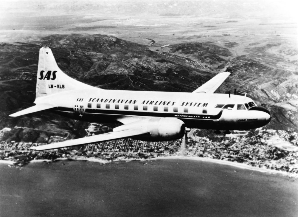 Luftfoto. Et fly, LN-KLB, Convair Metropolitan fra SAS, passerer over et tettsted på vei til neste destinasjon