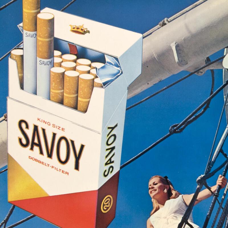 Reklameskilt. En pakke sigaretter i forgrunnen. En dame om bord på en båt i bakgrunnen