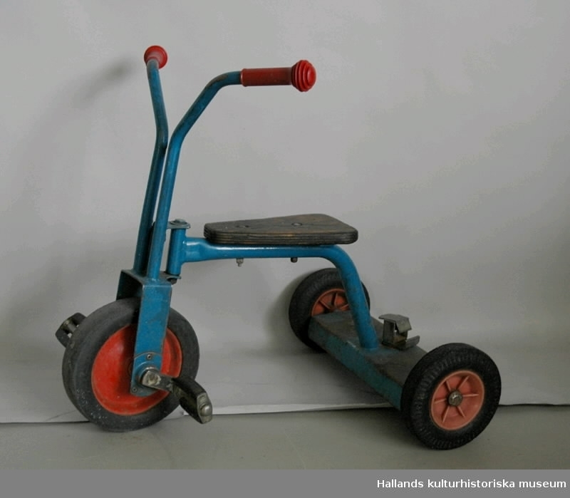 Röd och blå trehjuling med plasthandtag och träsits.
