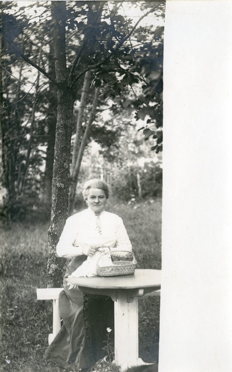 Marie Høyer sitter ved et bord i en hage. Hun holder sysaker i hendene.