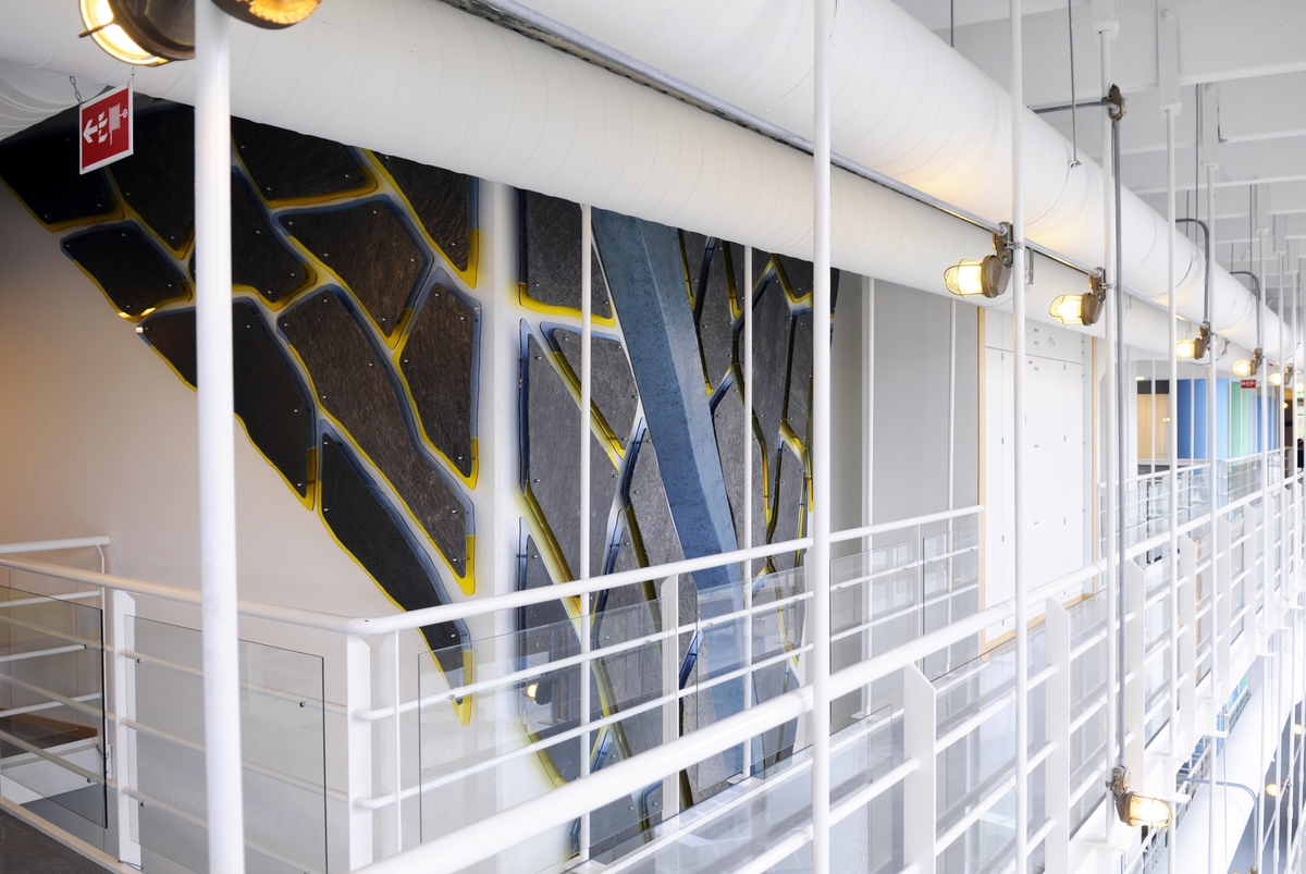 Vegginstallasjonen går over 3 etasjer og består av en hel hovedform som er støpt i glassfiber. Denne formen "tegner" bevegelsen i verket. Langs hele formen, på begge sider, er det montert skiferformer med en synlig "kontur" av farget plexiglass i gult og blått.