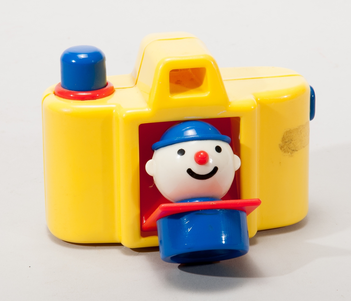 Leksakskamera i gul plast, linsen fälls ner när man trycker på utlösaren och ett clownhuvud visas då.