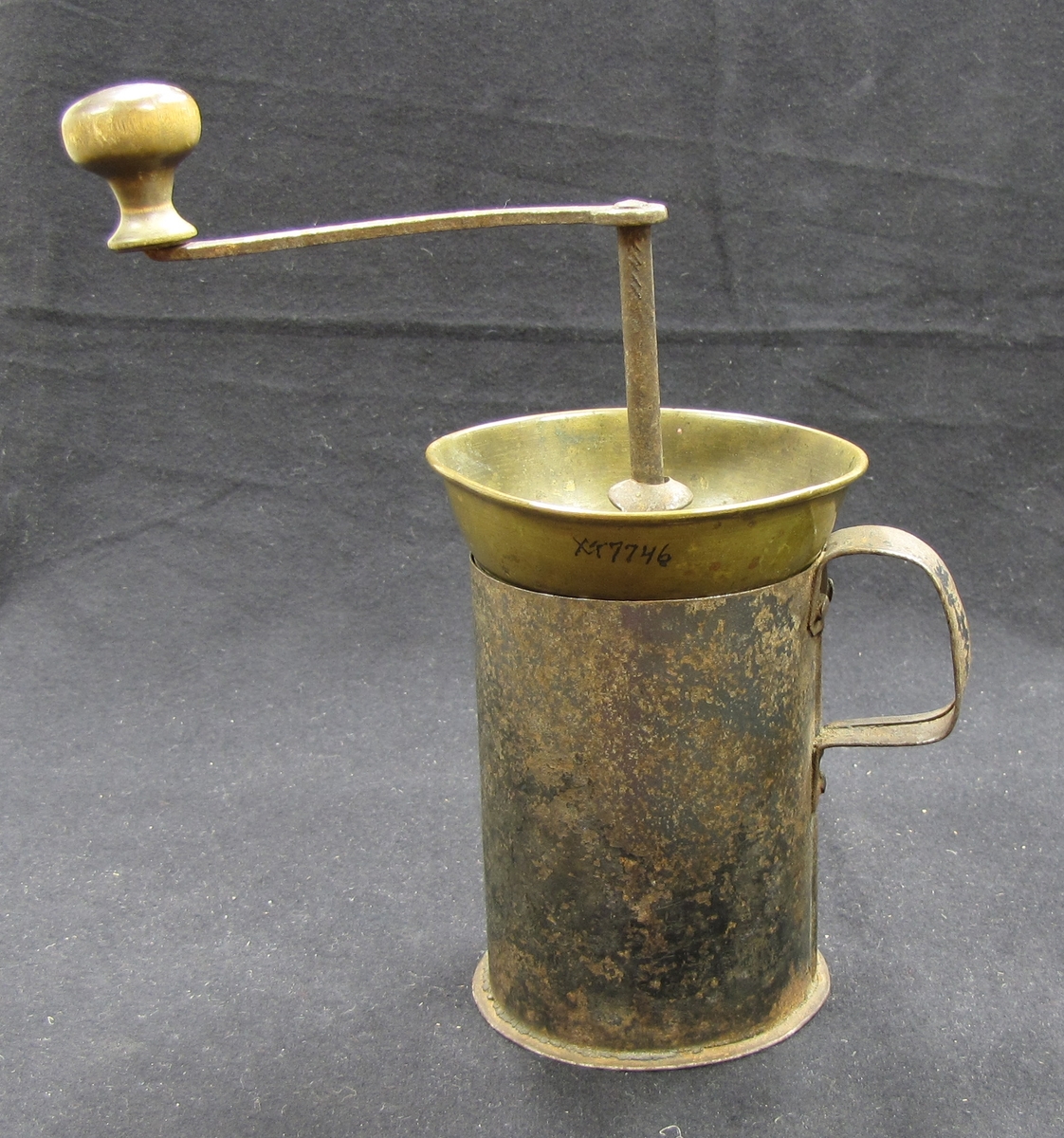 Kaffekvarn med vev med trähandtag. Tratt av mässing. Behållaren består av en mugg i plåt med handtag. Kaffekvarnen användes för att mala kaffebönor till pulver.
