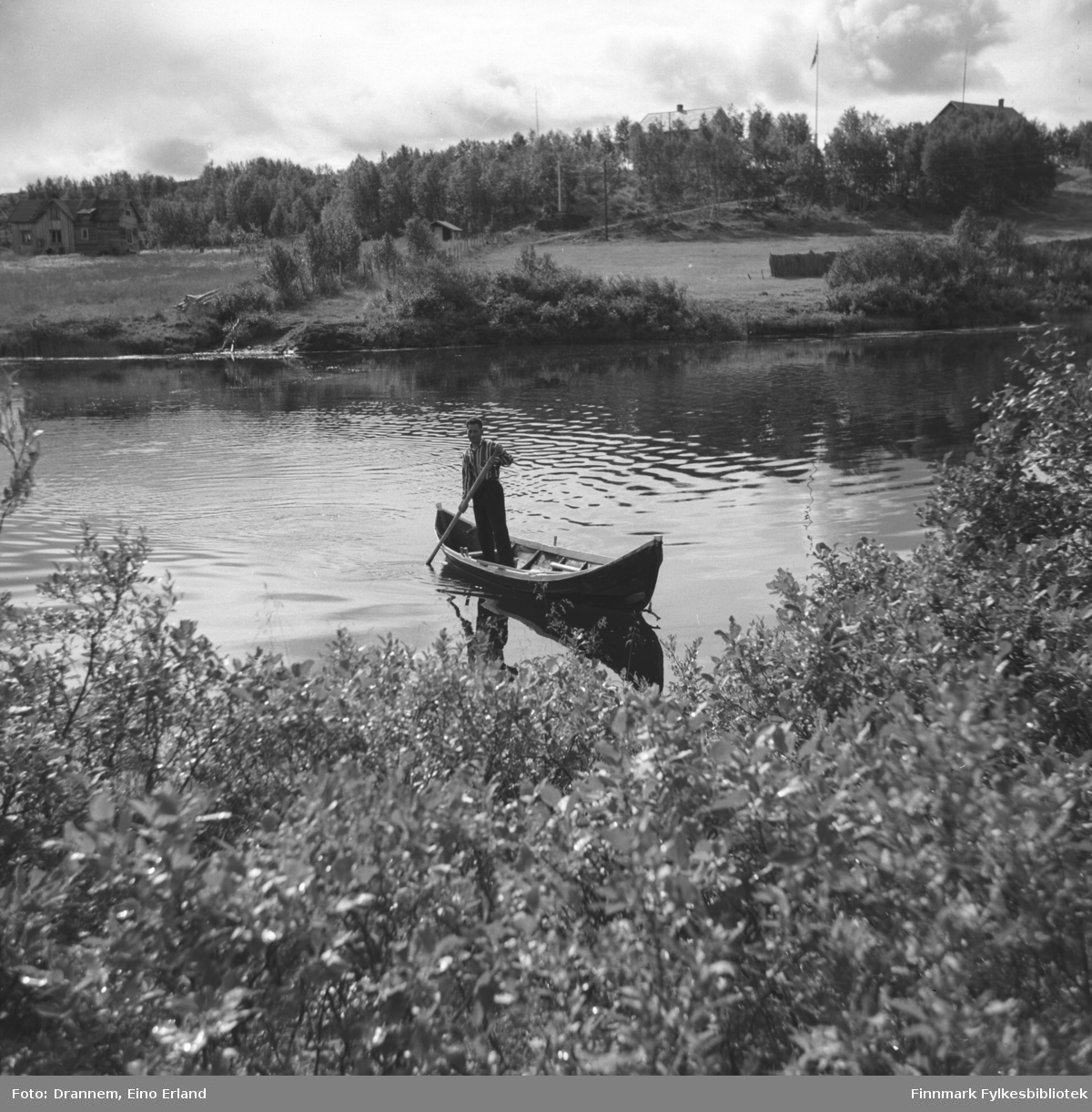 Neidenelva rundt 1950-1960. Olav Gabrielsen står i en elvebåt, "Neidenbåten", og staker mot land. 
