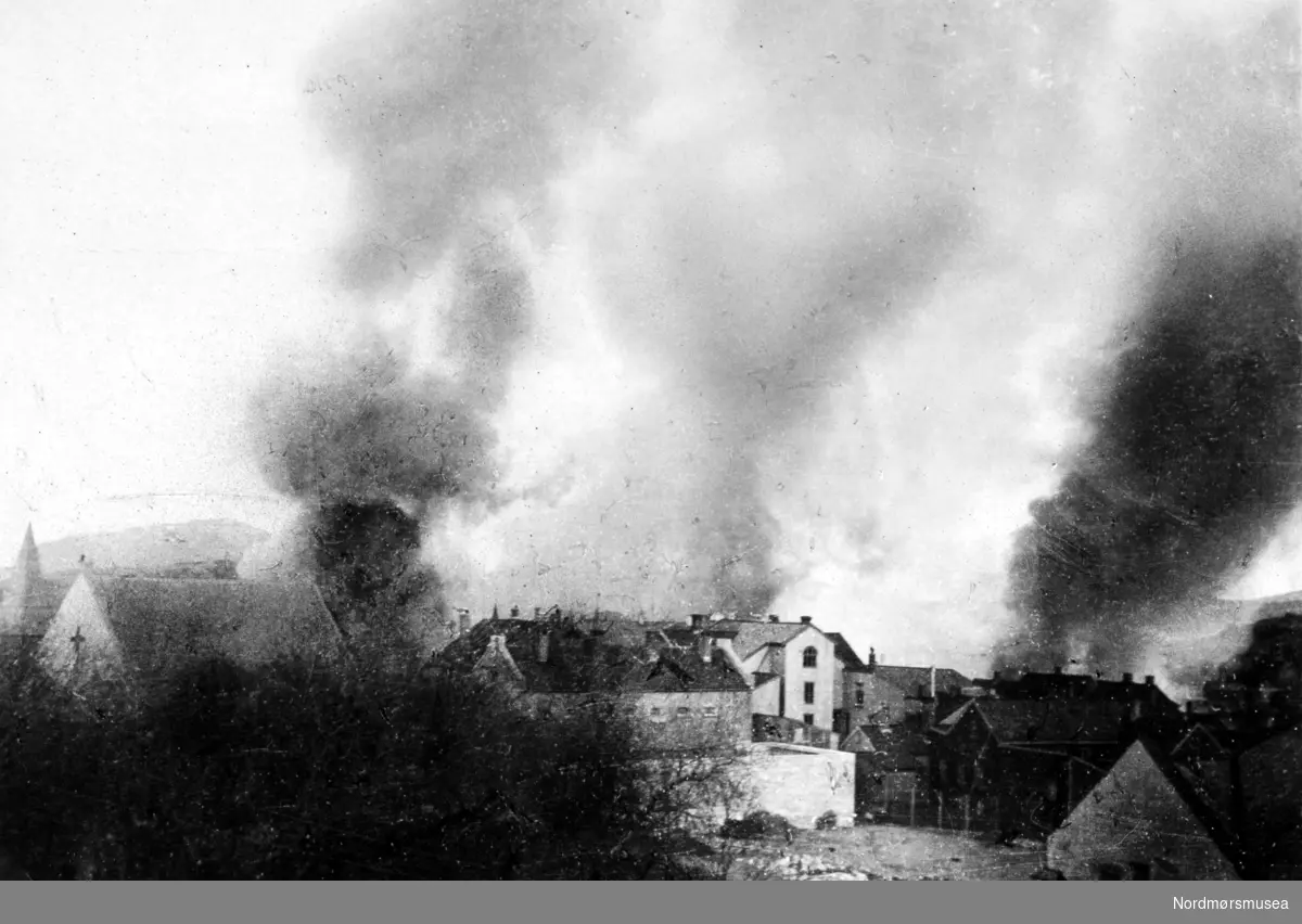 Andre verdenskrig har kommet til Kirkelandet i Kristiansund. Her ser vi det brenner på Kirkelandet. Bildet er fotografert fra Parkhaugen, og datert 29. april 1940, som er andre dagen med hvor byen ble bombet. Bildet er stemplet Monge foto. Fra Nordmøre museums fotosamlinger.