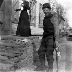 Foto av en mann med fisk stående ved en penere kledt kvinne 