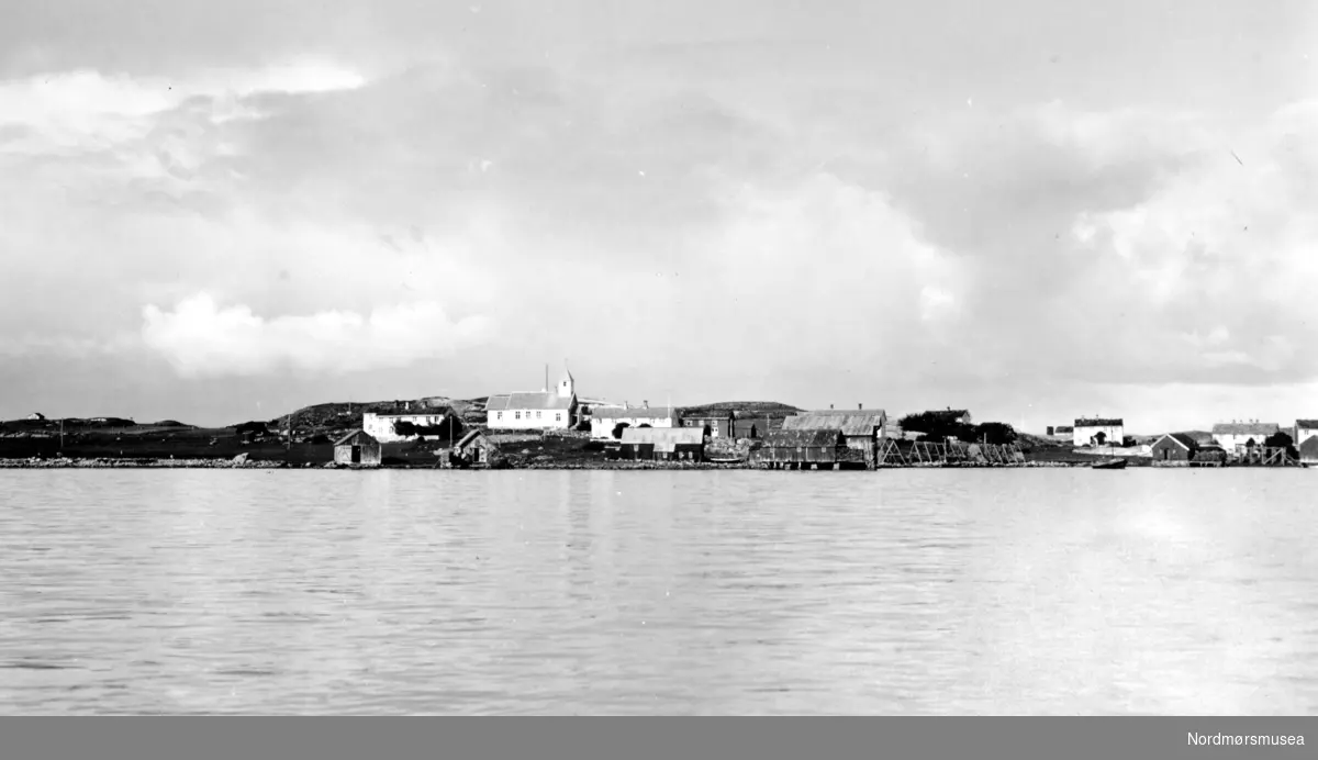 Parti fra Langøy, trolig i Averøy kommune, sett fra sjøen. Her ser vi blandt annet brygger og andre sjøhus, samt ei kirke til venstre på bildet. Datering er 1935. Se også KMb-1987-005.1306. Fra Nordmøre Museums fotosamlinger. Reg: EFR
