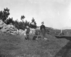 Foto av en kvinne og to gutter med håndvogn, stående ved sid