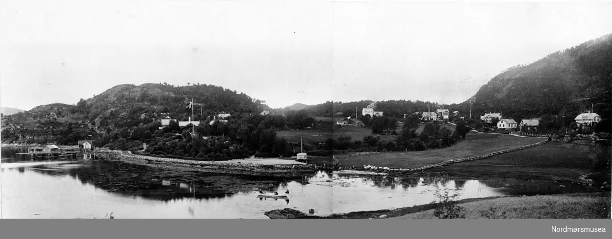 Panoramafoto fra ei bygd, hvor vi ser ei elv i forgrunnen og bebyggelsen i bakgrunnen. Det er også ukjent når bildet er tatt, men trolig omkring 1920 til 1939. Fra Nordmøre museums fotosamlinger.
