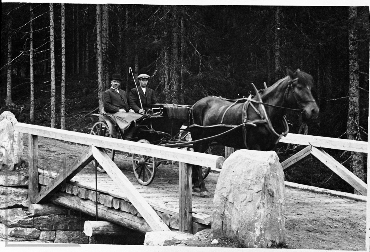 Inge Iversen og Guvald Felberg kjører over ei bru med hest og vogn.