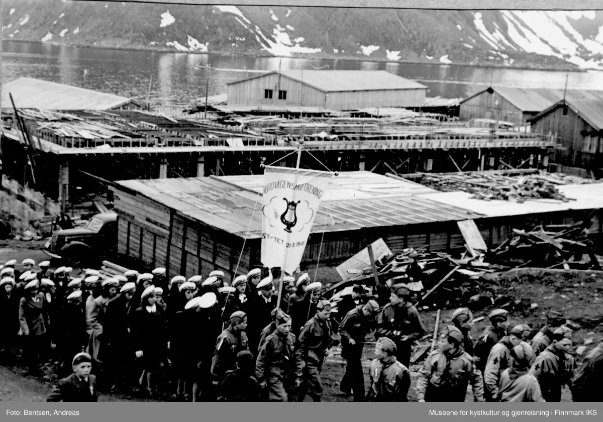 Gjenreisning. Honningsvåg. 17.mai-tog forbi Kolstadbygget (materiallager). Brakkebebyggelsen. 1947.