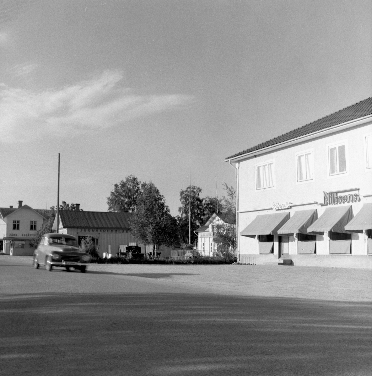 Någonstans i Värmland - från slutet av 1950-talet. Kommentar från en användare:"Bilden är tagen på Kyrkheden, Ekshärad med Nilssons möbel- och kappaffär och Järnbolaget. Längst bort är Pressbyrån och Richenbergs affär".