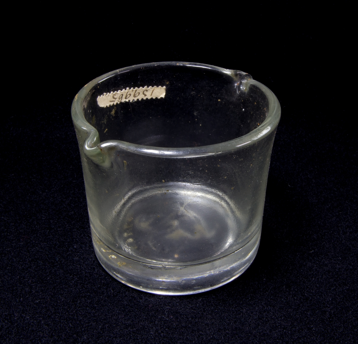 Glas, cylindriskt, genomsiktligt med två uthällningspipar. Under botten märkt med en svan i relief i glasmassan.