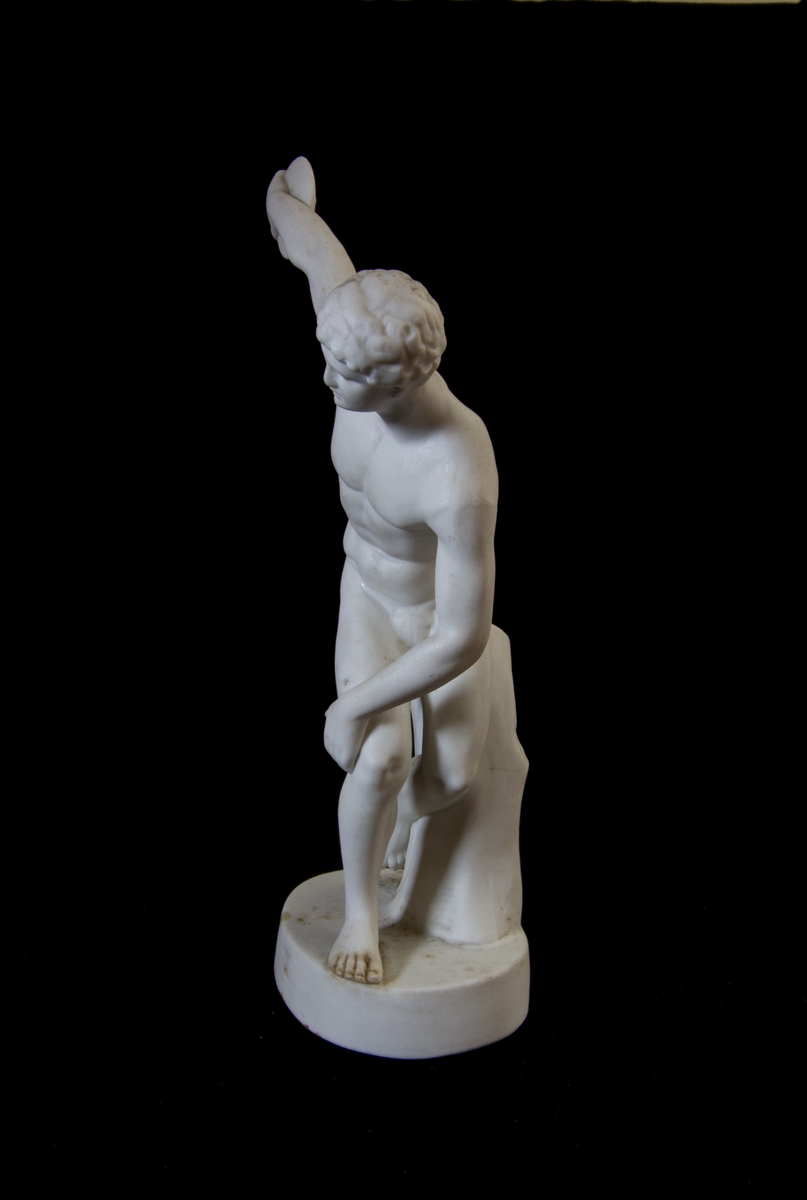 Studiemodell i parian föreställande en naken man i helfigur som håller en diskus i sin bakåtsträckta hand. Lutar sig delvis mot ett stubbliknande föremål. Oval fotplatta.
