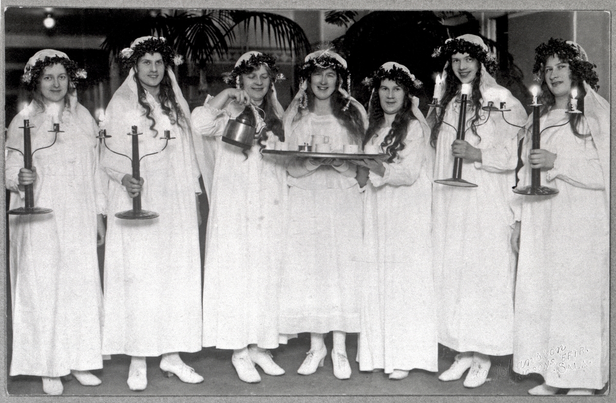 Luciafest på Sala lasarett 1921 med skämtsamt inslag. Lucia i mitten med bricka i hand omgiven av sina tärnor. Deltagarna i tåget är sannolikt personal på lasarettet som ska uppvakta patienterna.