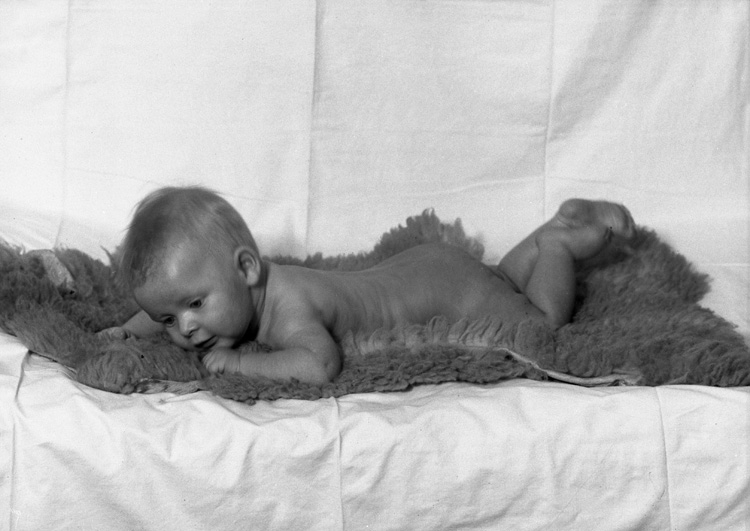 Ett litet naket barn ligger på mage på en fårskinssfäll.