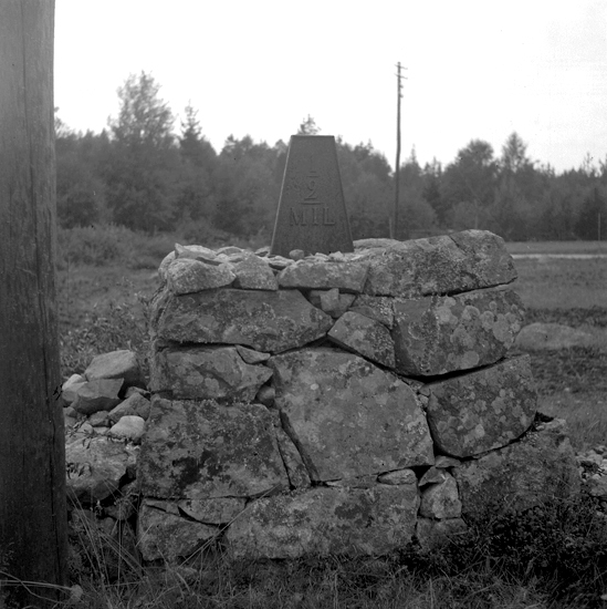 Foto av en milsten av järn, med röse. 
Text: " 1/2 MIL."
1000 m NNV om Älmeboda station. 1 m V om vägen. 
Vägen Linneryd-Älmeboda. 
Källa: Kronobergs läns väginventering 1943.