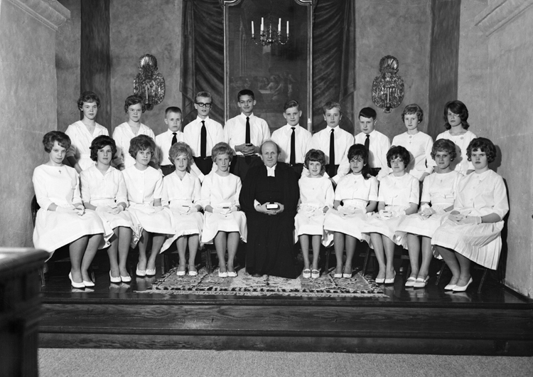 Foto av en konfirmationsgrupp med konfirmandpräst som är församlade i koret till Aringsås (Alvesta) kyrka.