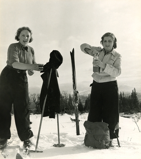 Två unga kvinnor i sportkläder tar en kafferast under
en skidtur.
