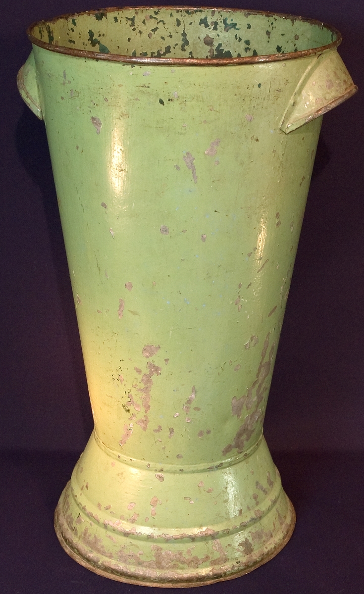 Vas av grönmålad bleckpåt för snittblommor att exponera blommorna i vid försäljning.
Färgen delvis bortnött.