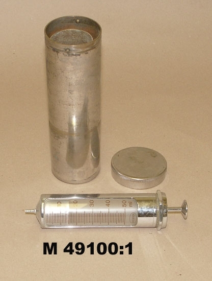 Injektionsspruta.
Okänd tillverkare i Schweiz på 1950-1960-talen.
Använd av veterinär fram till början av 1980-talet.
Beskrivning: Injektionsspruta i förnicklad mässing med förvaringscylinder.
Sprutan har glassidor med graderingen 1-50 ml. 
Det graderade glaset är märkt. Se "Signering, märkning" 1 ovan.
Det andra glaset är märkt "Standard 50", "PAT 200 C BREV, STERILISATION STERILIZATION; ZUSAMMENGESETZT FULLY ASSEMBLED, INTERCHANGEABLE KALIBRIERT 200 C" (grader celsius).
Förvaringscylinder i förnicklad mässing med lock och bajonettfattning samt lättrad kant. Armerad gummipackning fastskruvad på lockets insida med plåtbricka.
Locket märkt "H-SALBY" på utsidan. Inuti cylindern finns en fjäderförsedd hållare för sprutan för att förhindra stötar.
Inskrivet i huvudkatalogen 2005-03-29.
Funktion: Injektionsspruta för veterinärt bruk.