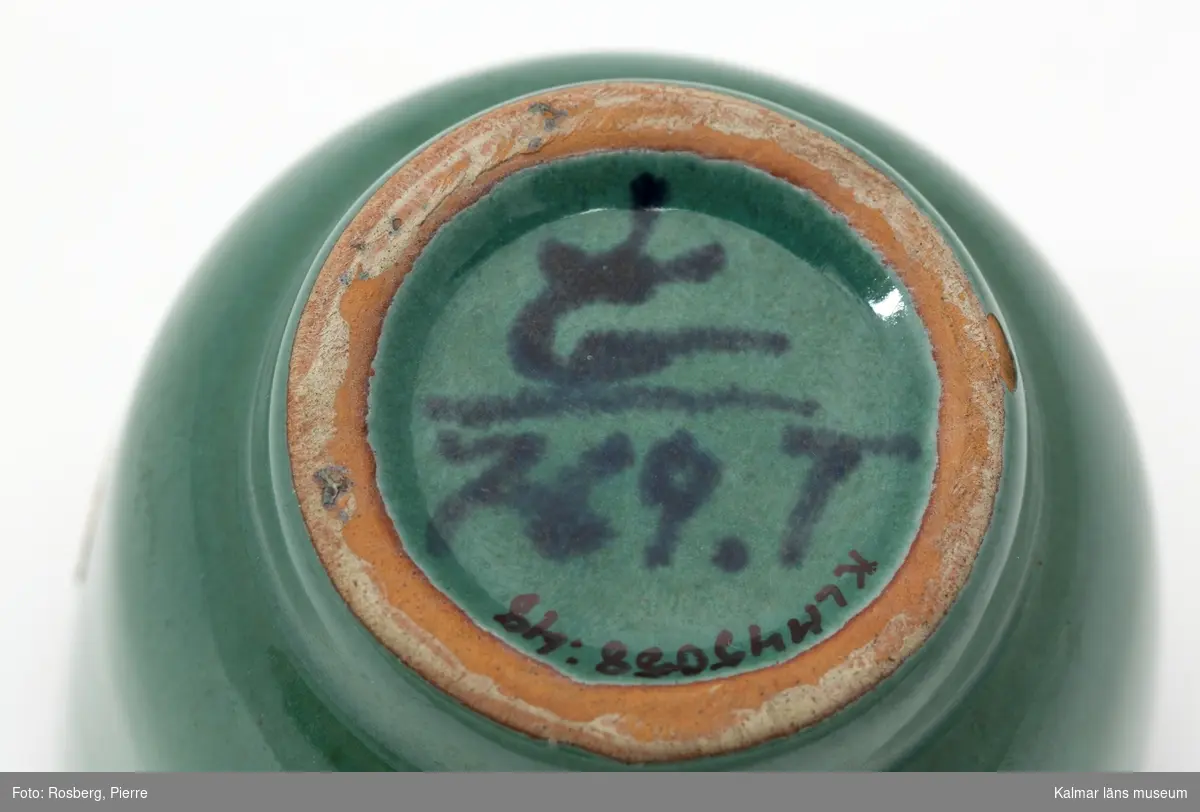 KLM 45058:48. Cigarettställ, av keramik. Cigarettställ av grönglaserad keramik med mörkare gröna tecken som dekor. Etikett på utsidan, Gabriel. På undersidan målad stämple, krönt G, samt 769.T. Ingår i en serie som kallades Broque, serien tillverkades i både grön och brun glasyr. Tillverkat av Gabrielverken. Datering, 1930-tal.