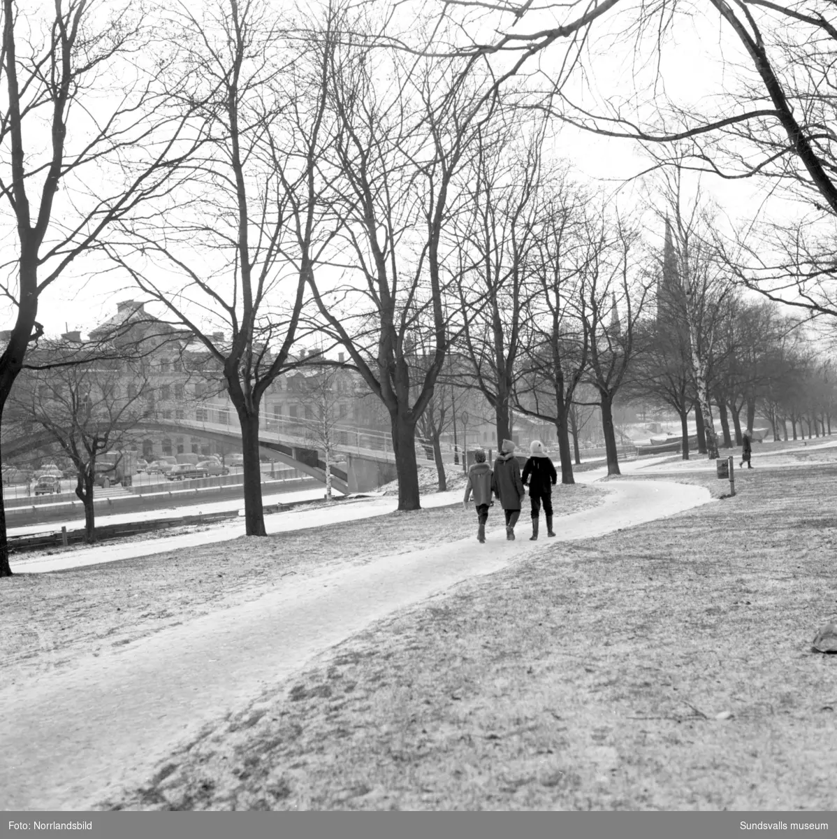 Vintervy från östra Norrmalm mot puckelbron. Tre barn på promenadvägen.