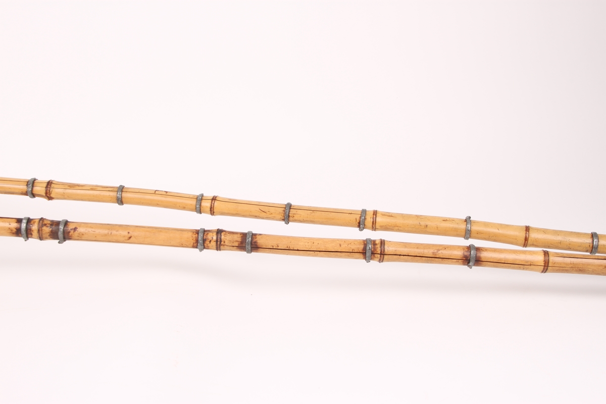 Et par bambusstaver med monogram brent inn øverst ved håndtaksremmen i lær. Staven er forsterket med ringer av blylegering. Flettverk-trinser bestående av røde skinnremmer og fettlærsremmer er festet til en dobbel trinsering av spanskrør.