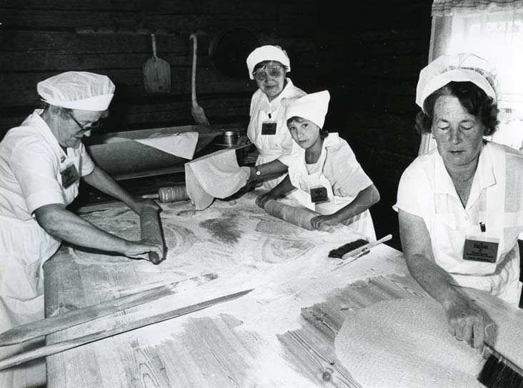 Tre kvinnor och en flicka bakar tunnbröd i en bakstuga.