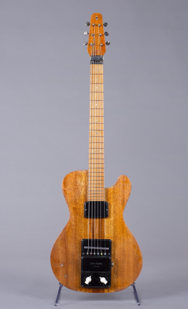 Elektrisk gitar med kropp og hals av mahogny. Magnet ved halsfeste og pickup ved strengefeste (NilsensSystem). Kontrollere for tilpasning og klangfarge. Tilpasning tilsvarer volum og gir størst volum på nivå 1. Enkelte av stemmeskruene er ikke originale.
