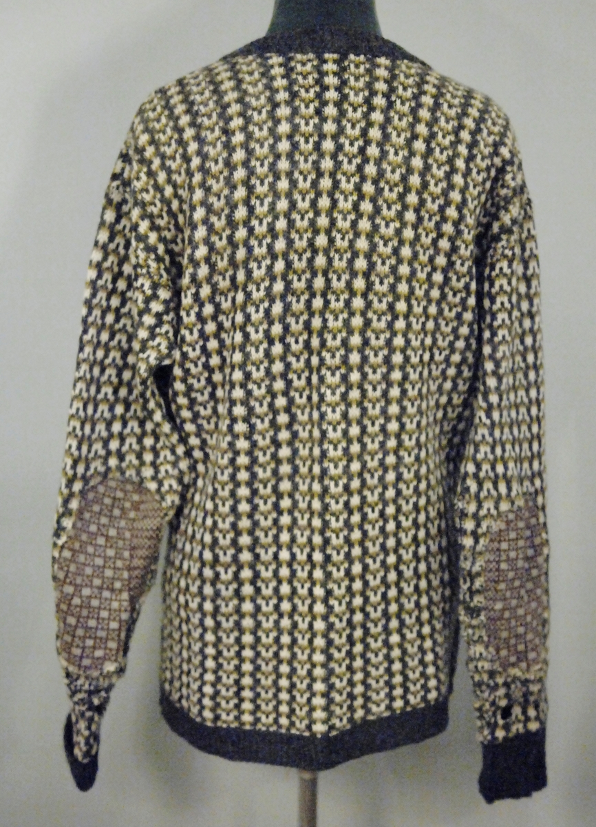 Ullgenser med v-utringning, grå/hvit med gult mønster. Innfelt stykke på albuen fra en annen genser, brunt og hvitt. 