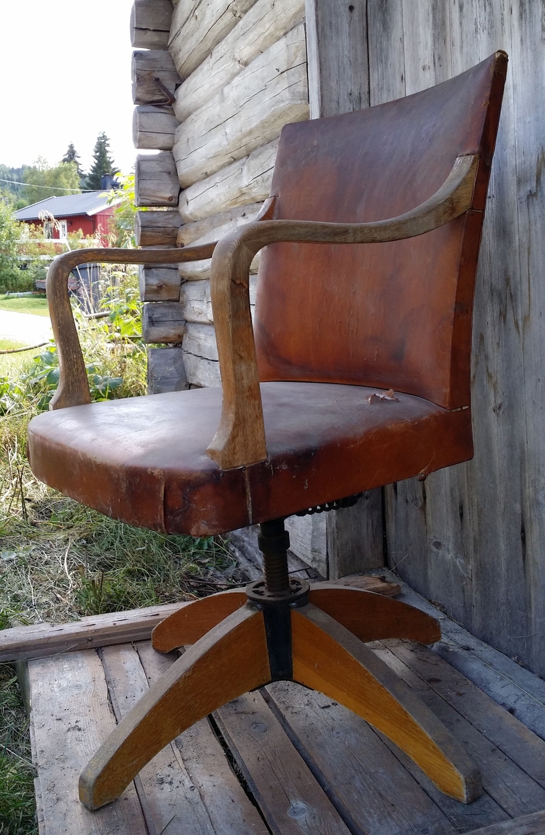 Stolen i  eik fra 1920-tallet har vært lakkert. Den er fjærbelastet og har originaltrekk i lær. Det er hull i trekket og en liten sprekk i siden på stolen.
