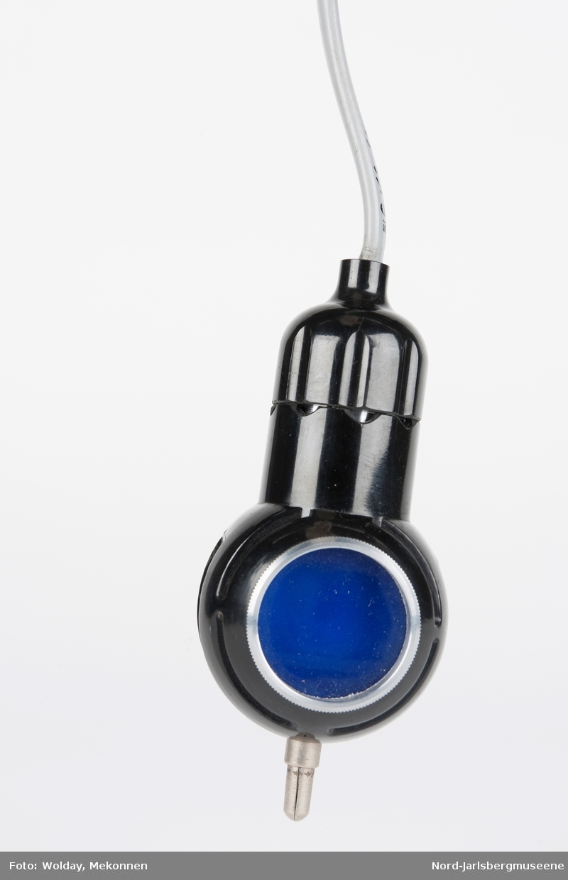 En liten lampe med to sider; en med blått lys, en med dempet lys. På toppen en metallpinne (el-kontakt?)Nyere ledning med bryter påmontert. Usikker bruksmåte og formål.