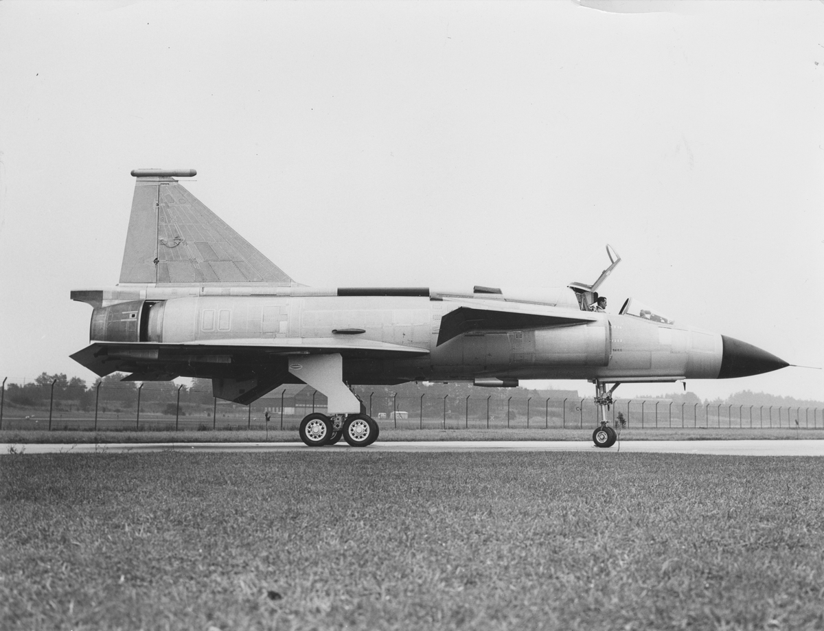 Prototypen för flygplan Saab 37, nummer 37-1 står på ett fält. Flygplanet är omärkt. I förarsitsen sitter en man.