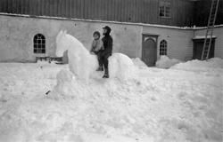 To barn som sitter på en snøskulptur i form av en hest. Bild