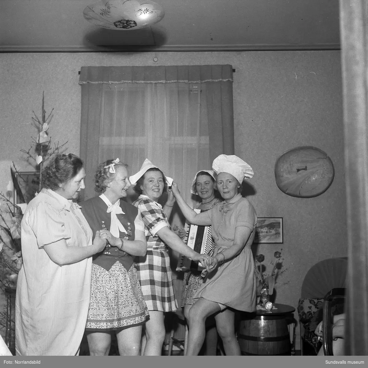 Humoristisk julgransplundring med sex glada damer i en syjunta (Fredriksson). En av kvinnorna spelar dragspel.