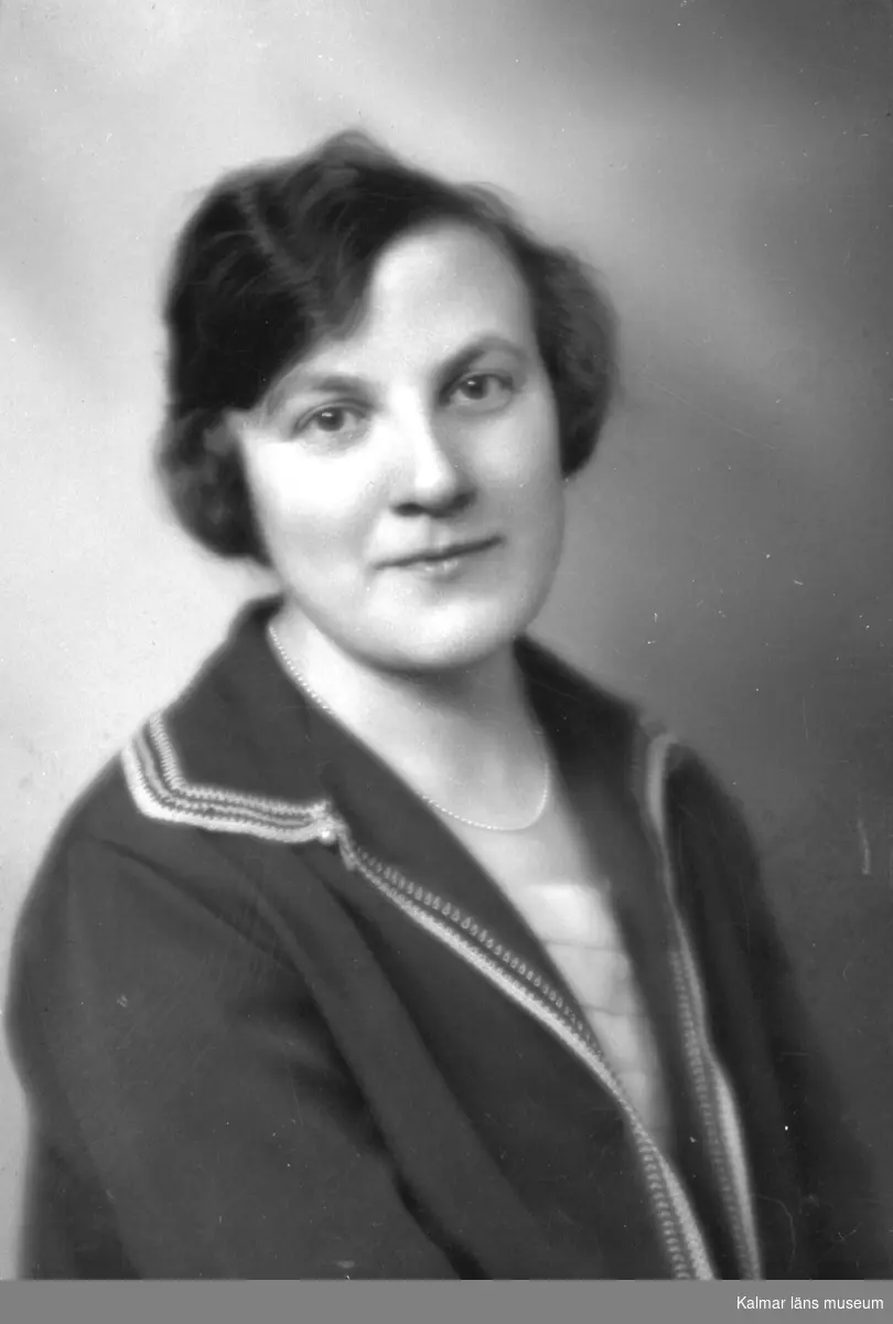 Ateljébild på en kvinna i jacka och halsband. Beställare till bilden: Fröken Elsa Göransson ifrån Nybro.