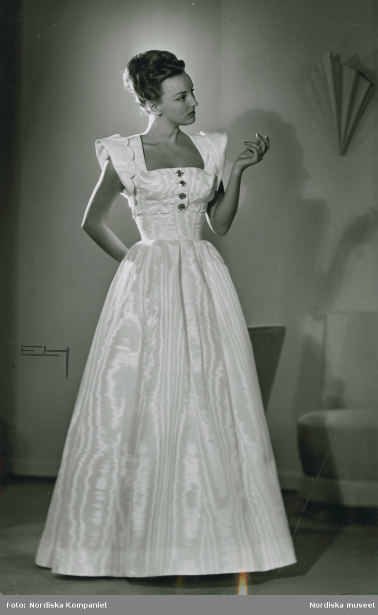 Modell, möjligen Hjördis Grundel-Starenius,  i vit aftonklänning med utställd kjol.