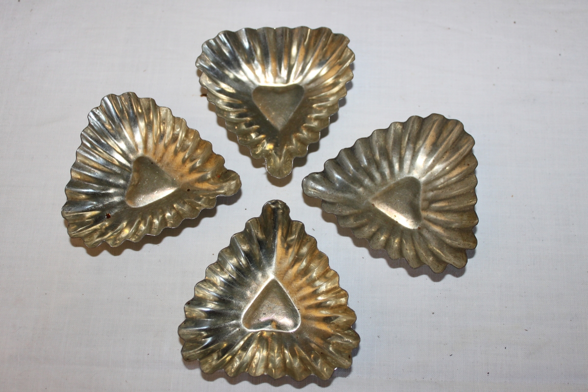 Fyra Hjärtformade kakformar i plåt för mandelmusslor och liknande bakverk.