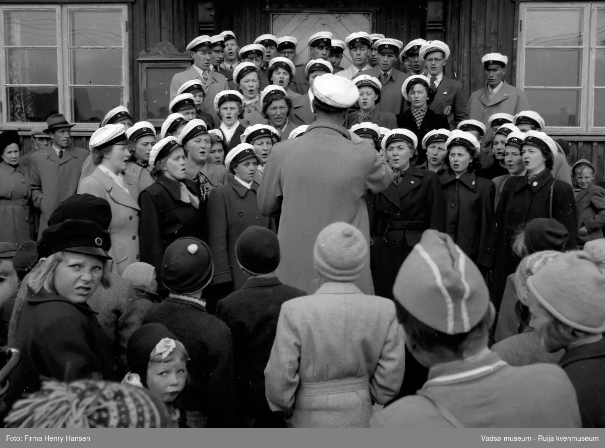 Vadsø sentrum 17. mai 1951. Korsangere foran postbrakka. Barn og voksne er tilskuere.