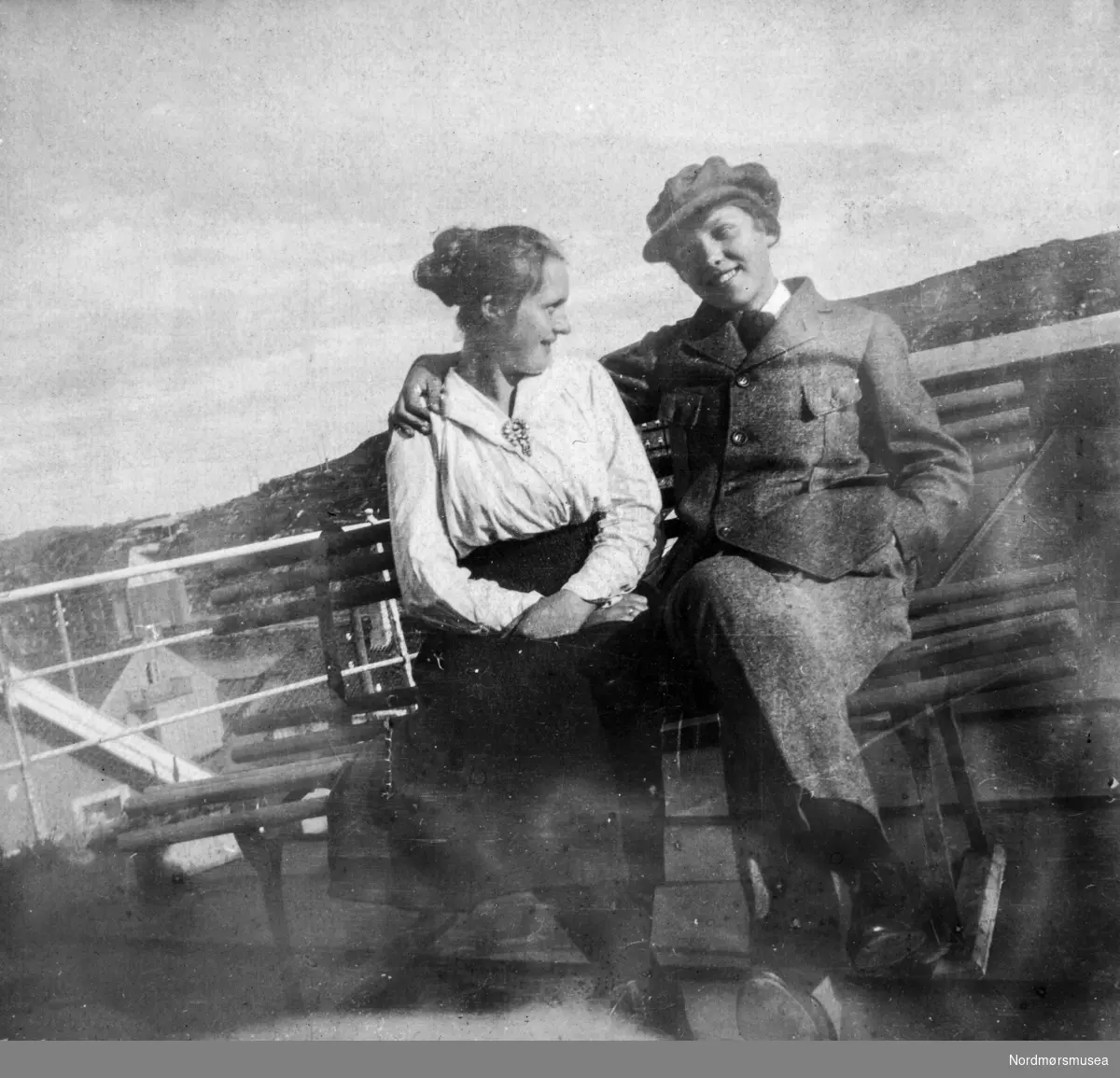Gruppebilde av to personer sittende sammen. Bildet er trolig fra Kristiansund omkring 1918-1920 og de vi ser på bildet er sannsynligvis fra Williams-familien. Fra et fotoalbum tilhørende Ellinor Williams-Phakdikun (1905-1963). Fra Nordmøre museums fotosamlinger.